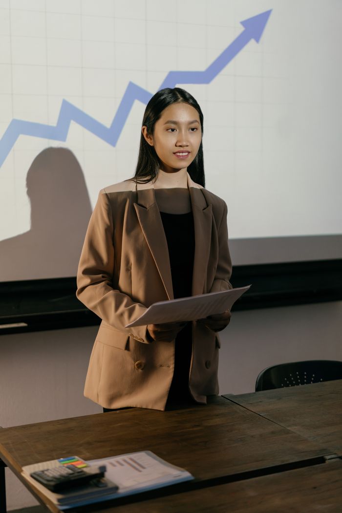 Confident businesswoman in a blazer presenting data with a rising graph in the background.